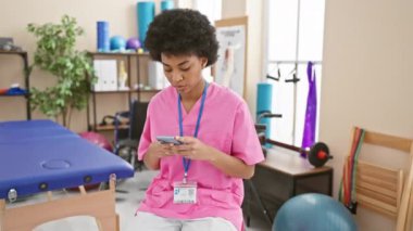 Kendine güvenen Afrikalı Amerikalı kadın, gülümsüyor, rehabilitasyon kliniğindeki akıllı telefonundan mutlu bir şekilde mesaj atıyor.