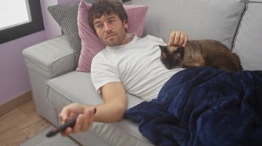 Rahat bir adam, rahat bir şekilde kanepede uzanır. Uzaktan kumandayla siyam kedisini okşar. Kapalı bir odada rahat bir sahne tasvir eder..