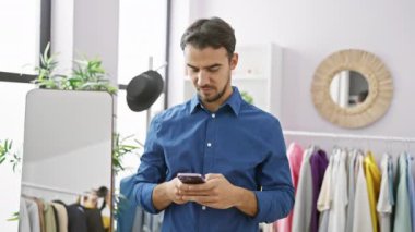 Yakışıklı, mavi gömlekli adam modern giyinme odasında elbise askısı olan akıllı telefon kullanıyor..