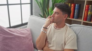 Düşünceli, genç İspanyol bir adam oturma odasındaki kanepede oturuyor, parmakları çenesine, derin düşüncelere dalmış, şüpheyle boğuşuyor, evdeki harikalar dünyasında kayboluyor..