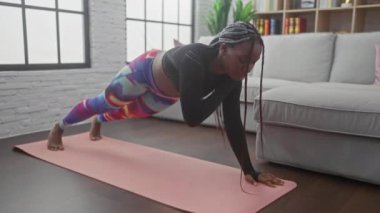 Örgülü zenci bir kadın modern bir oturma odasında yoga yapıyor.