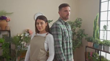 Çapraz kollu çiçekçi ve kendine güvenen erkek ve kadın çiçekçiler yapraklı bir çiçekçide duruyorlar..