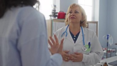 Bir hastane odasında yaşlı sarışın kadın doktor kapalı klinik ortamında bir hastayla tokalaşıyor..