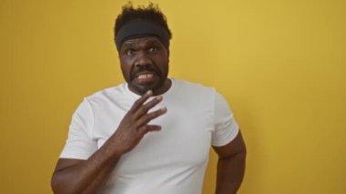 Beyaz tişörtlü afro-amerikan adam şok oldu ve korktu, ağzı kapalı, şaşırmış bir ifadeyle izole edilmiş sarı arka planda.