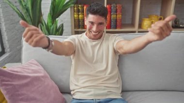 Neşeli, genç İspanyol bir adam, evdeki koltukta oturuyor, sıcak bir kucaklama için kollarını ardına kadar açıyor. Yakışıklı bir erkek kameraya neşeli bir gülümseme, mutluluk ve sevgi saçıyor.