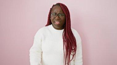 Süslü, gözlüklü, beyaz kazağı pembe bir duvara dayanmış Afrikalı bir kadın..