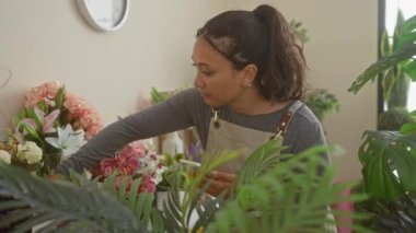 Önlük takan İspanyol bir kadın akıllı telefon kullanırken parlak bir çiçekçide çiçek ayarlıyor..