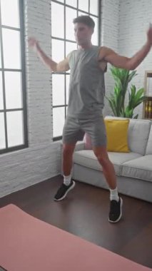 İspanyol adam oturma odasında yoga minderi, kanepe ve doğal ışıkla egzersiz yapıyor.