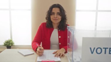 Kırmızı kazaklı genç bir İspanyol kadın oy pusulasını şeffaf bir oy sandığının yanında doldururken kapalı bir seçim kurulunda oy kullanıyor..