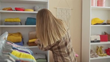 Parlak, modern bir gardıropta renkli kıyafetler düzenleyen genç bir kadının arka görüntüsü..