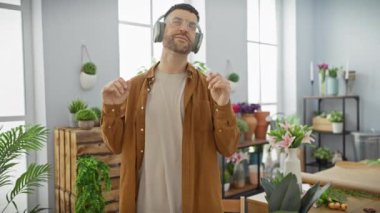 Çiçekçide sakallı, kulaklıklı İspanyol bir adam dans ediyor.