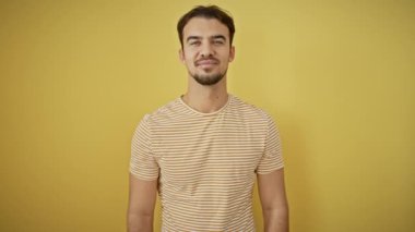 Çizgili tişörtlü, zaferi sevinçle kutlayan genç İspanyol bir adam. Elleri başarıyla havaya kalkmış, neşeli bir ifade, parlak sarı izole edilmiş bir arka plan..