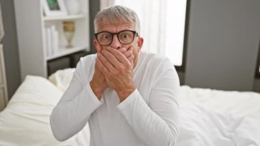 Şok olmuş orta yaşlı, gri saçlı, pijama giyen, ağzı ellerle kaplayan, yatak odasında yanlış sırlar açığa çıkan,.