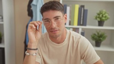 Neşeli, genç, İspanyol bir adam gözlüğünü iyi döşenmiş bir evde ayarlıyor, pozitifliğini ve gündelik tarzını ifade ediyor..