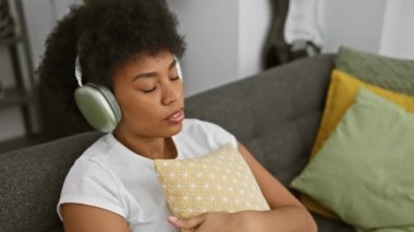Rahatlamış Afro-Amerikan kadın kulaklıklarıyla evdeki kanepede kestiriyor.