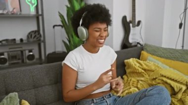 Mutlu siyahi kadın evdeki koltukta kulaklıkla müzik dinliyor..