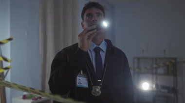 Rozetli odaklanmış bir adam suç mahallindeki bir odayı el feneriyle araştırıyor..