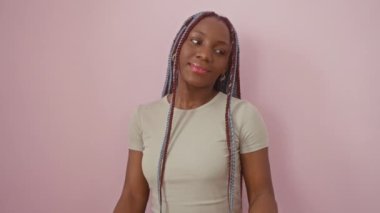 Gülümseyen Afro-Amerikan kadın şakacı bir şekilde geriye doğru işaret ederek izole edilmiş pembe arka planı onaylıyor.