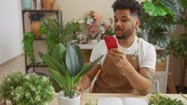 Afro-Amerikalı bir adam çiçekçide akıllı telefonuyla fotoğraf çekiyor.