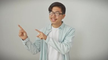 Gözlüklü neşeli genç Çinli adam yan tarafı göstererek, izole edilmiş beyaz bir duvarda hayali ürünler sunuyor, yüzünü kameraya doğru aydınlatan kahkahalar atıyor..