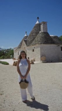 Beyaz elbiseli, gülümseyen İspanyol bir kadın mavi gökyüzünün altında, alberobello, puglia, İtalya, Avrupa 'da, geleneksel trulli evlerin önünde duruyor..