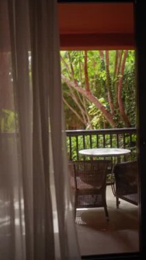 Perdelerin arkasından yemyeşil bir bahçeye bakan masa ve sandalyelerle balkona davet etmek.