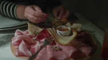 Bir kadın geleneksel İtalyan yemeklerini sıcak, kapalı bir restoran ortamında yer, et dilimleri ve ekmek malzemeleriyle lezzetli bir ahşap şarküteri tahtasının tadını çıkarır..