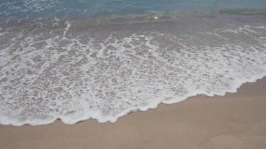 Sakin bir sahil sahnesi. Dalgalar, köpük, kum, güneş ışığı ve berrak su huzur verici sahil kenarı rahatlığını davet ediyor..