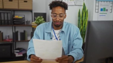 Ofis ortamındaki Afrikalı Amerikalı bir adam odaklanmış ve kutlama duygularını ifade eden belgelere bakıyor..
