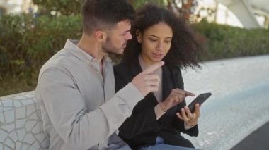 Güneşli bir günde, açık havada akıllı telefonu inceleyen bir kadın ve erkek şehir parkındaki modern ilişkinin örneğiydi..