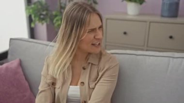 Genç sarışın kadın, kızgın ve kızgın bir şekilde koltukta oturmuş öfkeyle bağırıyor. Öfke ve agresif kavram. evde.