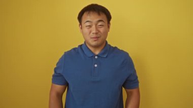 Başarıyı kutlayan genç Çinli adam zafer ve başarı için izole edilmiş sarı arka planda heyecanla ayakta duruyor ve çığlık atıyor.