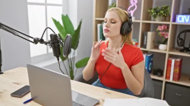 Genç sarışın bir kadın, mikrofona konuşurken duygularını ifade eden modern bir stüdyoda podcast yapıyor..