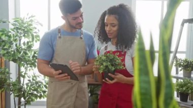 Bir erkek ve bir kadın, çiçekçiler, bir bitkiyi inceliyorlar ve bir çiçekçinin yeşil iç kısmında bir tablet kullanıyorlar..