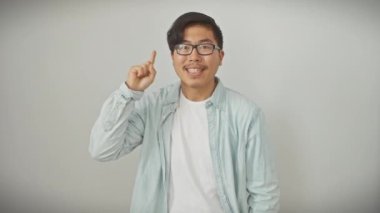 Genç Çinli gözlüklü adam ayakta durup başarılı bir fikirle işaret ediyor. Heyecanlı ve mutlu. Bir numara. izole edilmiş beyaz arkaplan