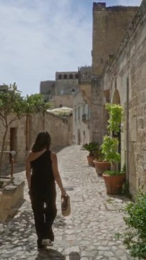 Genç bir kadın, dar kaldırımlı sokaklar, antik taş binalar ve parlak bir gökyüzünün altındaki yol boyunca canlı saksılarla İtalya 'nın çekici eski bir kasabasında yürüyor..