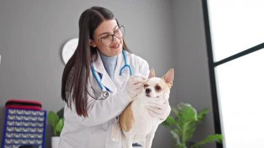 Veteriner kliniğinde köpek kulakları temizleyen, chihuahua köpeği olan genç İspanyol kadın.