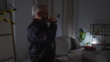 Bir adam, karanlık bir mekanda el feneriyle olay yerini inceliyor. Soruşturma ve şüphe hissi veriyor..