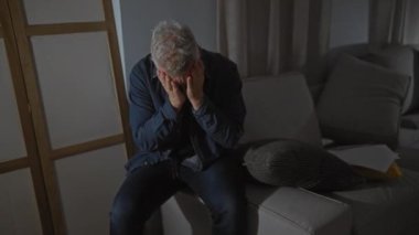 Beyaz saçlı ve sakallı üzgün bir adam. Kapalı bir yerde oturuyor. Yüzü korkunç bir şekilde kapanıyor..