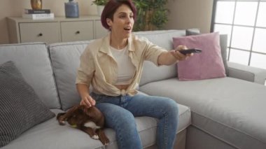 Genç bir kadın kanepede köpeğiyle oynarken oturma odasında televizyon izler..