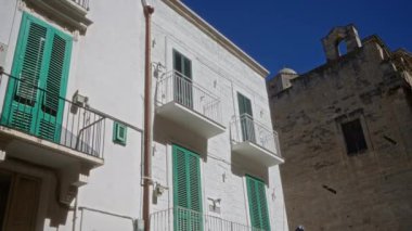 Puglia, İtalya 'nın güneşli caddesinde yeşil panjurları ve balkonları olan tarihi binalar canlı mavi gökyüzüne karşı geleneksel Avrupa mimarisini sergiliyor..