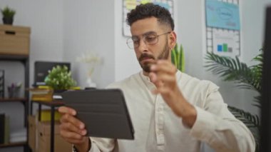 Modern bir ofiste çalışan genç İspanyol bir adam elinde bir tablet, profesyonel bir iş ortamında çalışıyor..