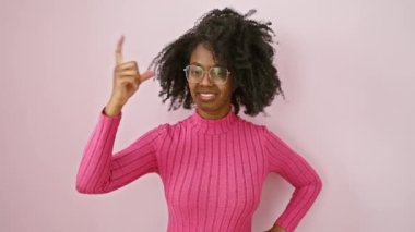 Gözlüklü kendinden emin Afrikalı Amerikalı kadın, küçük boy jesti sergiliyor. Pembe arka planda ölçü kavramı ile ayakta duruyor.