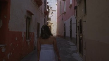 Beyaz elbiseli genç, İspanyol bir kadın Gelibolu, Puglia, İtalya 'da kırsal binalarla çevrili dar sokaklarda yürüyor..