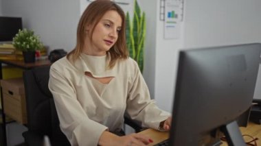 Ofisinde çalışan genç, sarışın, beyaz bir kadın. Kapalı bir odada bilgisayarla profesyonel ve çalışkan bir atmosfer yaratıyor..