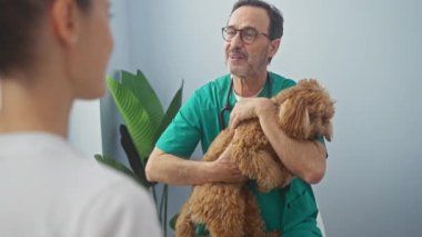 Klinikte bir kadınla görüşürken elinde kaniş tutan orta yaşlı bir veteriner..