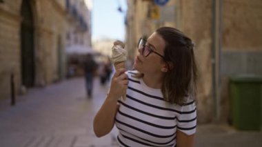 Genç İspanyol kadın güneşli bir günde Lecce, Puglia, İtalya 'da büyük bir dondurma külahının keyfini çıkarırken çizgili bir gömlek ve gözlük takıyor..