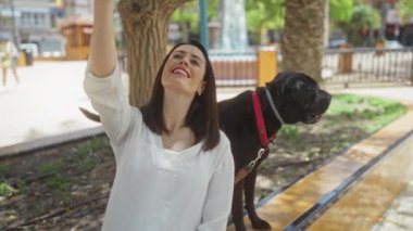 Genç İspanyol kadın güneşli bir günde köpeğiyle şehir parkında selfie çekiyor..