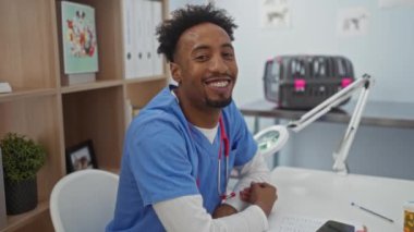 Önlük giymiş, veteriner kliniğinde gülümseyen, tıbbi aletlerle, defterlerle ve arka planda evcil hayvan taşıyıcılarıyla bir masada oturan Afrikalı genç bir Amerikalı..