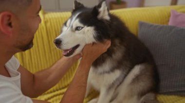 Genç bir İspanyol erkeği, samimi bir oturma odasında köpeğini sevgiyle besliyor. Bir anlık dostluk ve sevgi paylaşıyor..